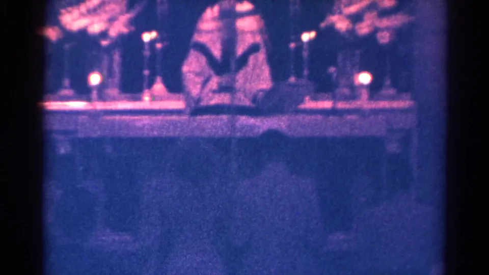In 1966 Danville, Illinois home-movie footage, a vested pastor appears at a candlelit altar reading from an open book.