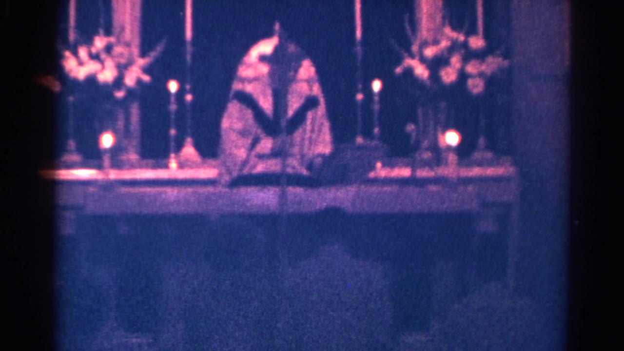 A pastor in vestments stands behind an altar in Danville, Illinois, with candles and floral arrangements framing the scene.