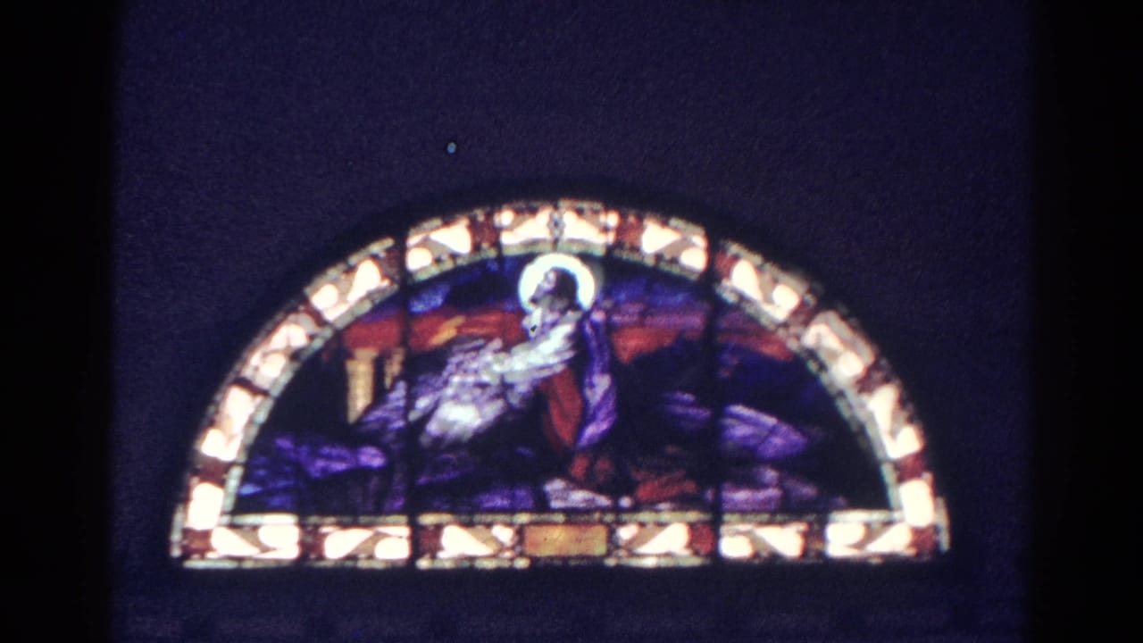 Arched stained glass window glowing in a dark church interior.