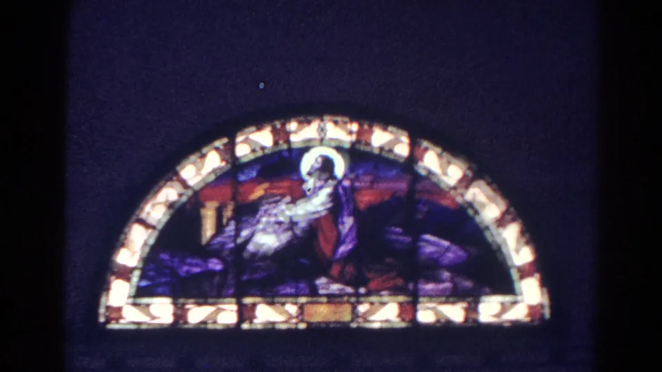 1966 Danville, Illinois 8mm frame of an arched stained glass window with a religious figure in a dim church interior.