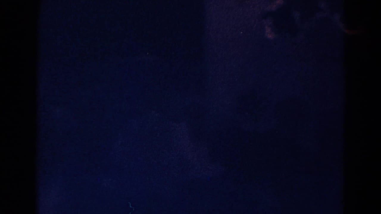 Dark 8mm frame from the Danville church clip, showing blue-black exposure, film grain, and little visible interior detail.