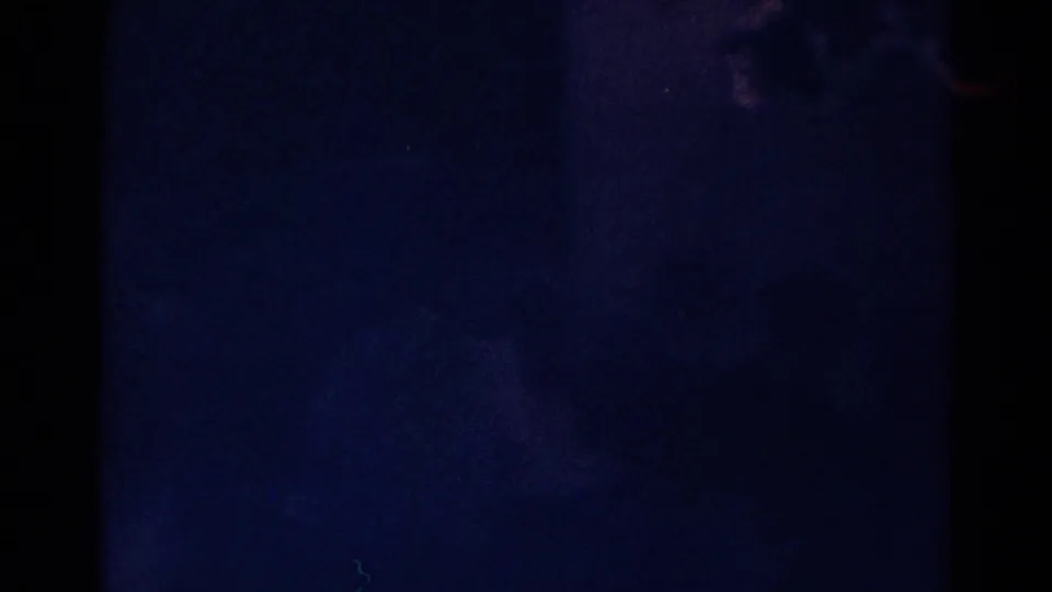 Dark 8mm frame from the Danville church clip, showing blue-black exposure, film grain, and little visible interior detail.
