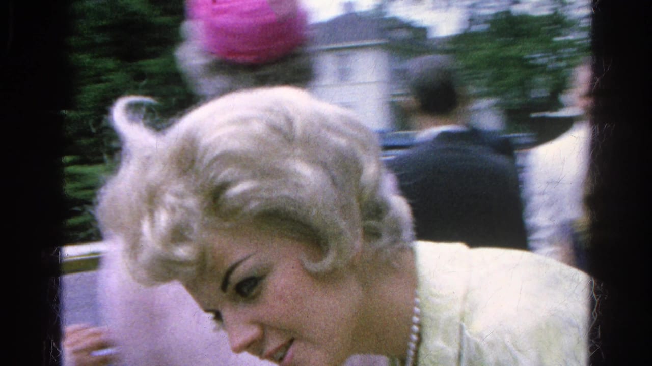 A blonde woman in a white jacket and pearl necklace leans forward among guests at the 1966 Danville outdoor gathering.