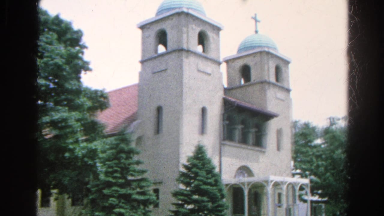 Light-colored church with twin towers and trees beside a quiet street.
