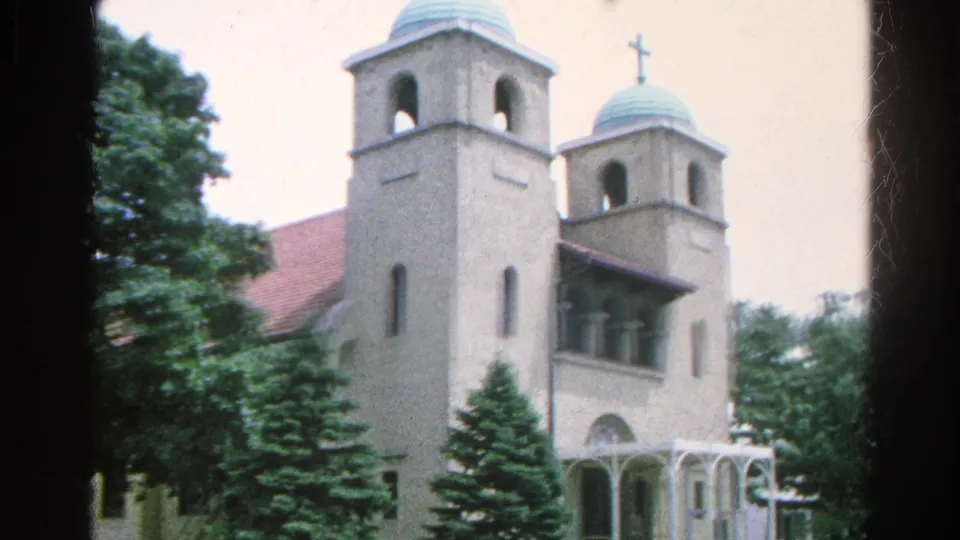 1966 Danville, Illinois home-movie frame showing a light-colored church with twin towers, green domes, trees, and a curbside street.