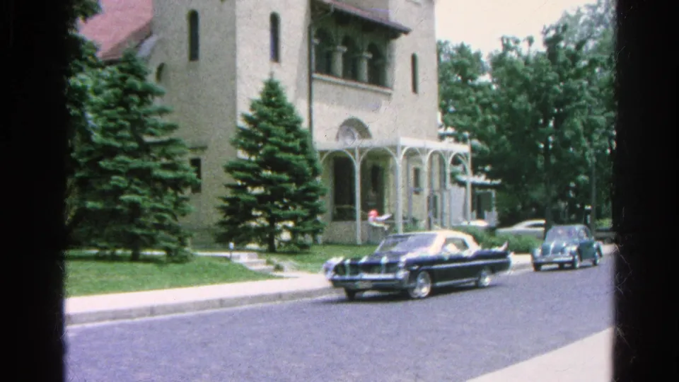 1966 Danville, Illinois street view with classic cars driving past a light-colored church and sidewalk in midday sun.