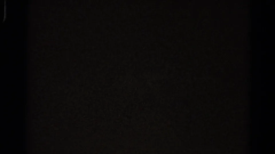 Dark 8mm frame from the clip, with only faint film texture and edge shadow visible.