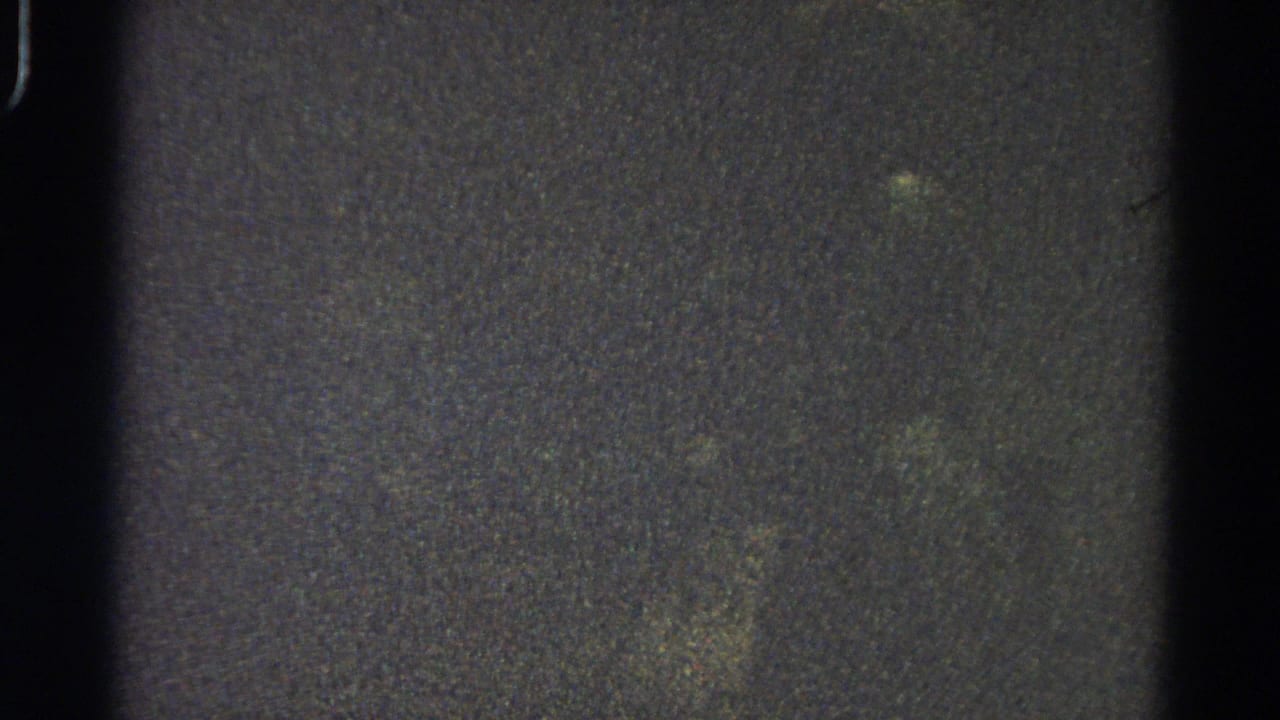 Grainy dark film frame with vertical black edge and mottled texture.