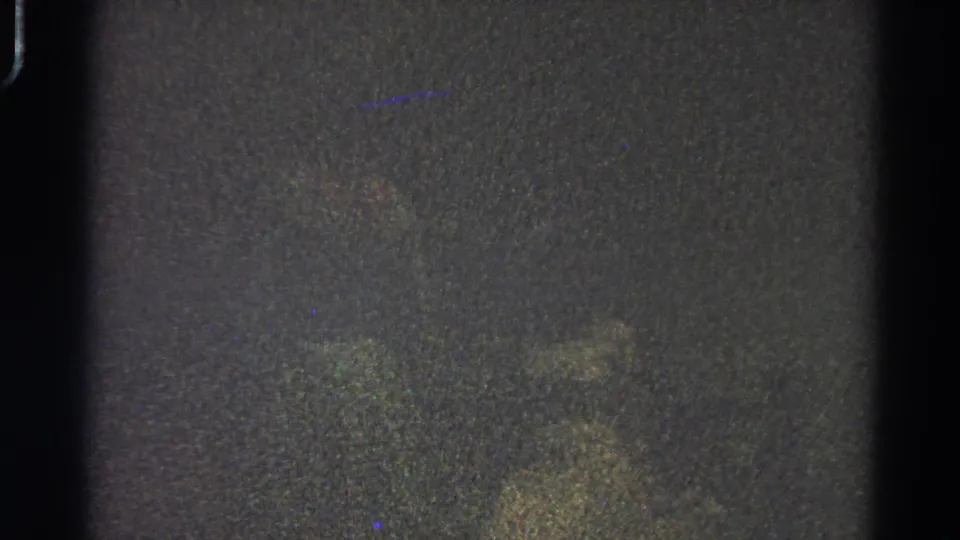 Dark 1966 Danville 8mm frame with dense grain, faint colored specks, and film-edge shadows, without visible figures or landmarks.
