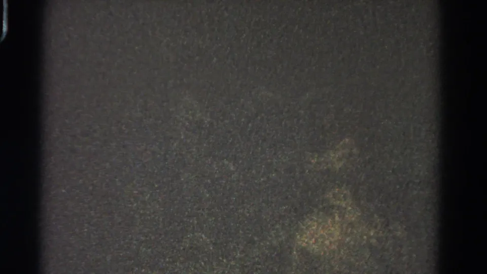 Underexposed 1966 8mm frame from the Danville wedding reel, showing grain, edge shadows, and faint mottled light with no clear subjects.
