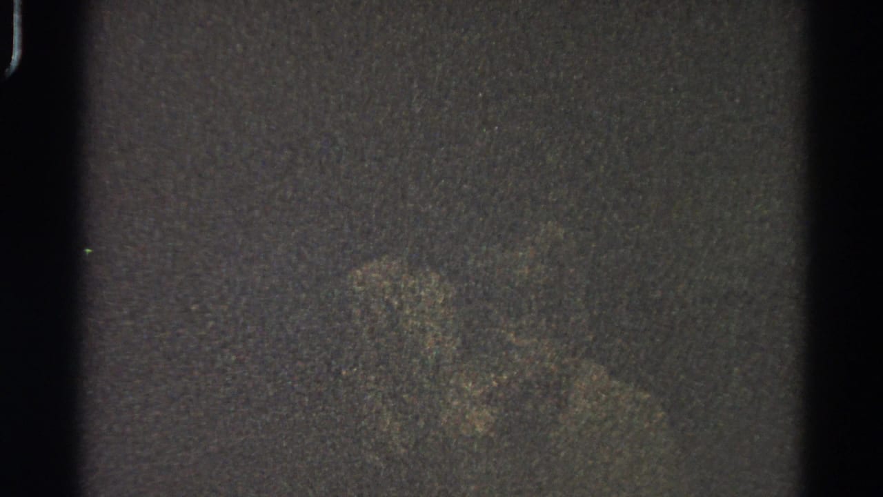 Dark grainy film frame with a faint central blur and visible vertical frame edges.