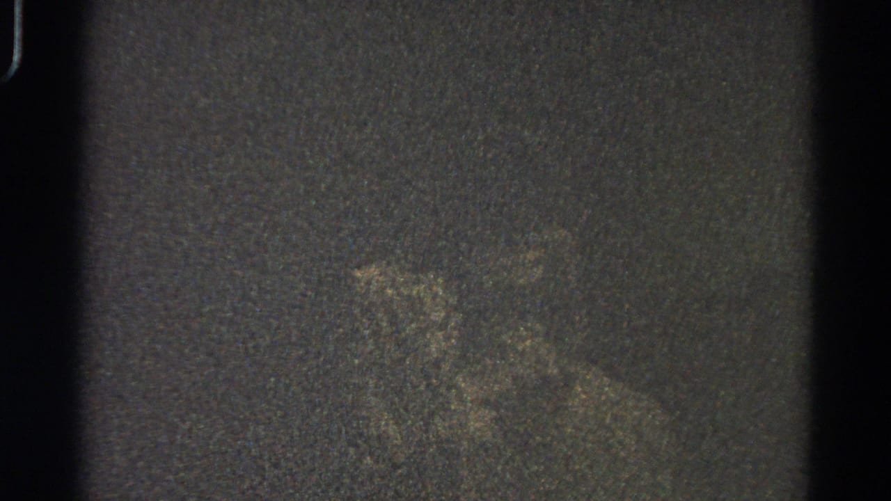 Low-light 1966 Danville 8mm frame showing a vague pale form against dark grain, with scratches and gate-edge artifacts.