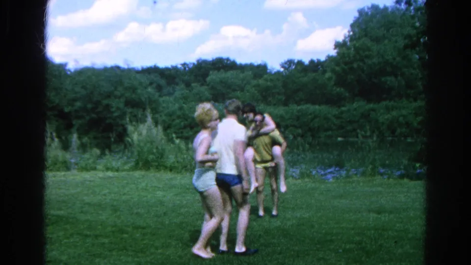 A 1966 Danville home-movie frame shows the group moving across grass during playful outdoor activity beside the pond.