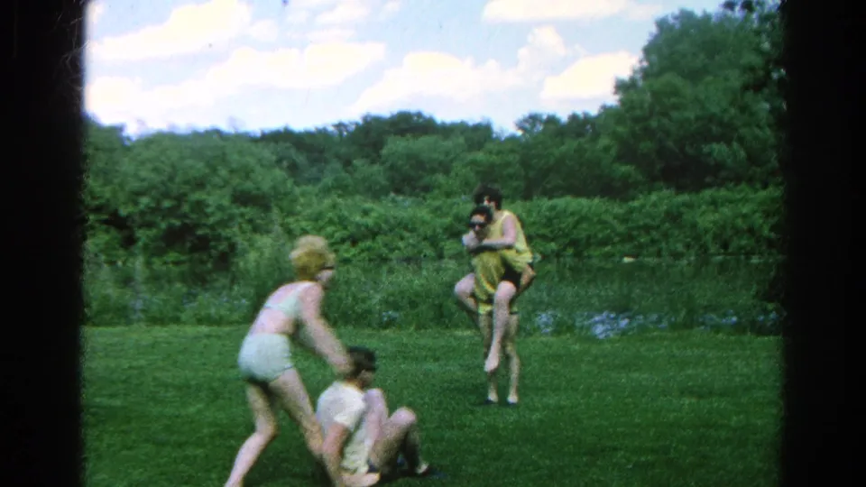 Danville, Illinois 1966 home-movie frame of young adults in swimwear and casual clothes playing on a lawn near water.