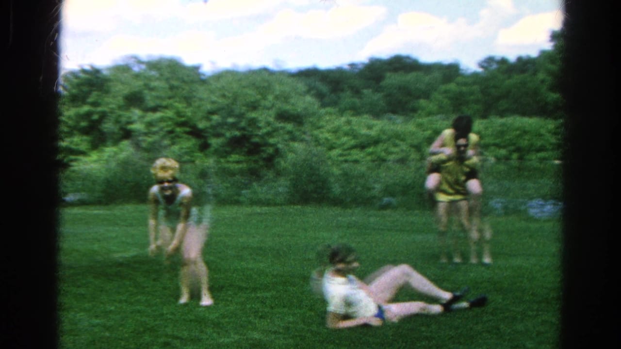 Two people give piggyback rides while another person sits on the grass.
