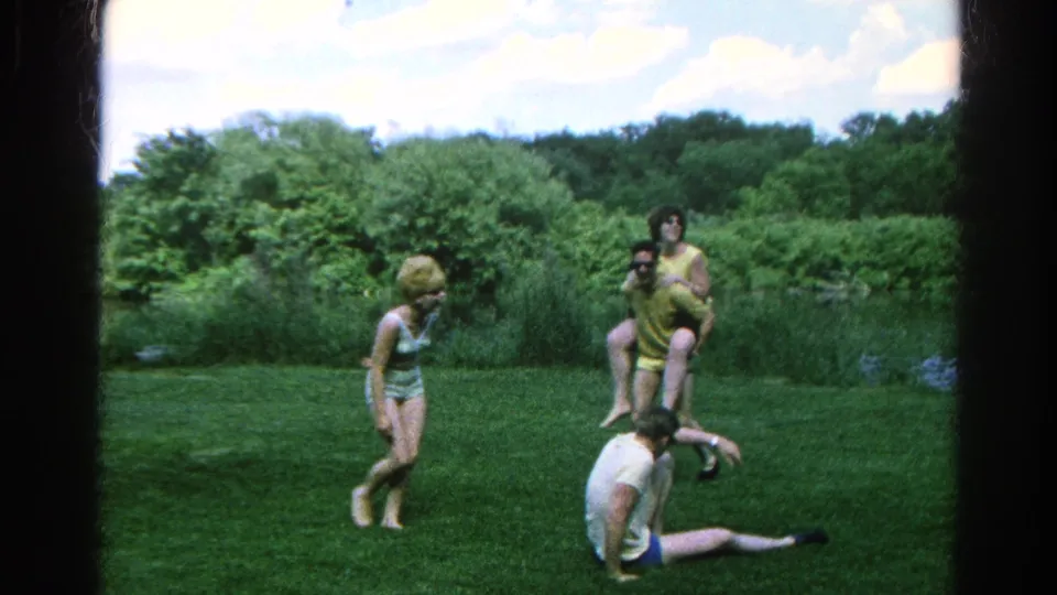 Danville 1966 frame showing young adults in swimwear and casual clothing regrouping during lawn horseplay near a pond.