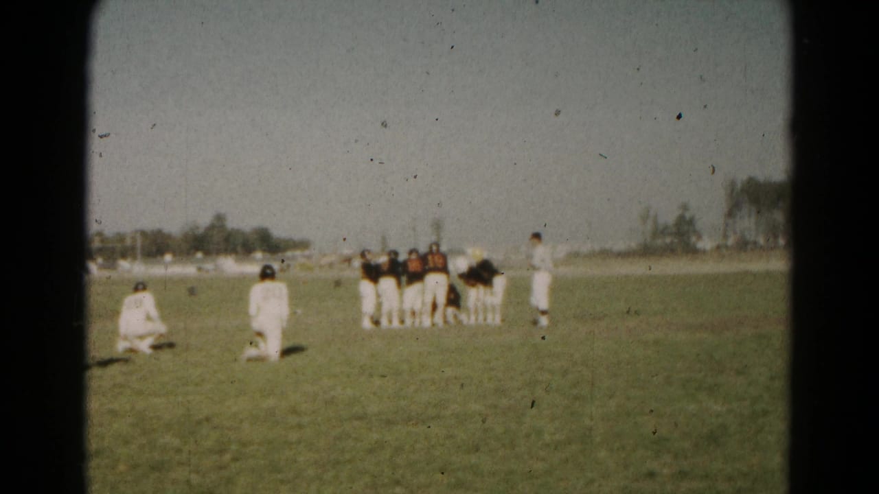 Youth football players gather on a grassy field, with two players kneeling in the foreground.