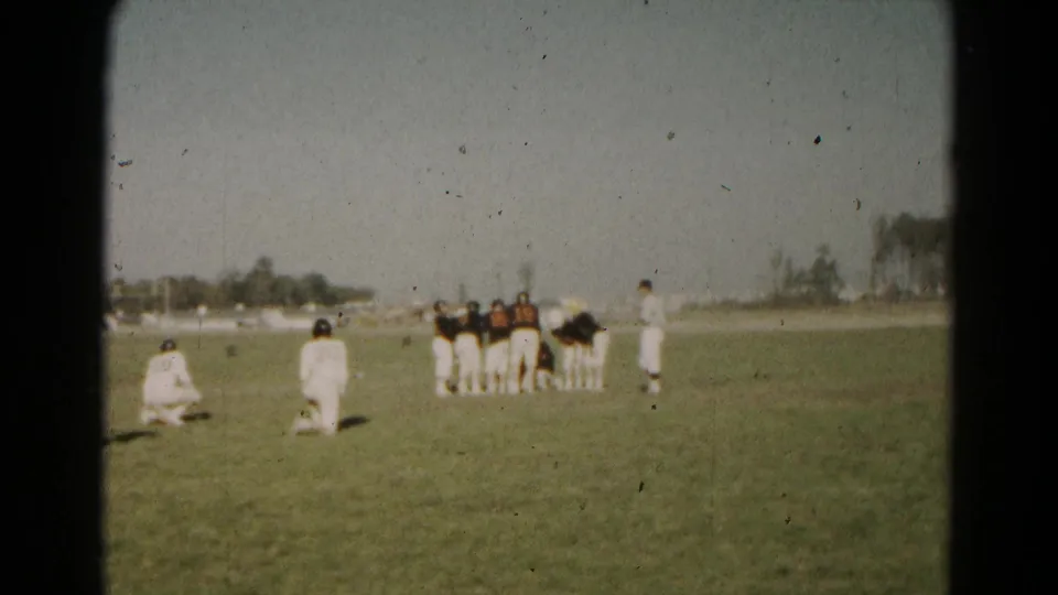 1966 Hagerstown home-movie frame showing youth football players in white and dark uniforms grouped on an open grass field.