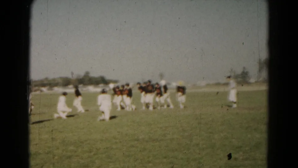 1960s home-movie frame showing youth football players shifting position during a play on a Hagerstown grass field.