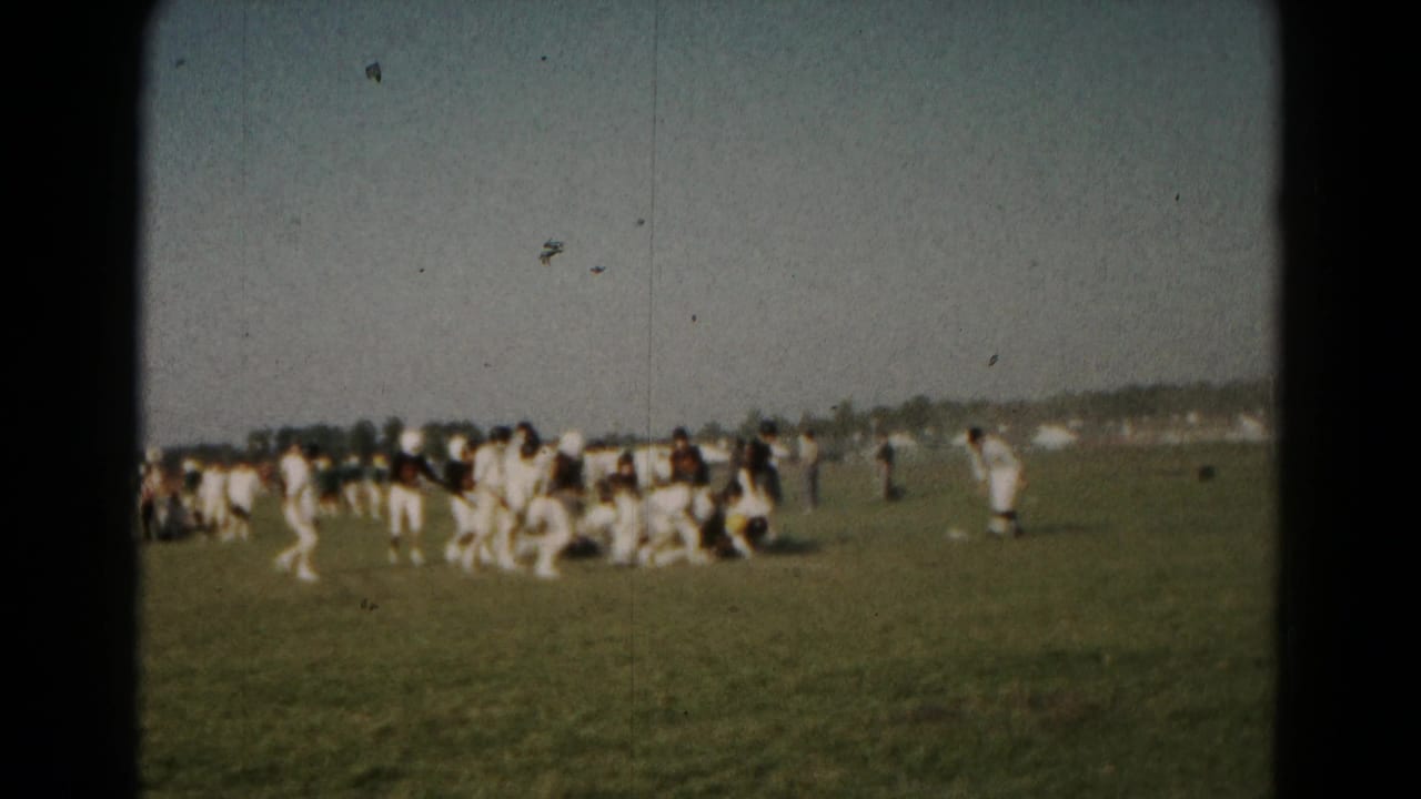 Players move around a tackle during a football game on grass.
