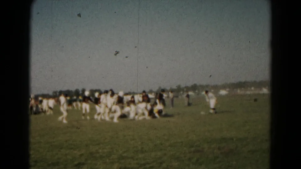 1966 Hagerstown frame with players converging around a tackle on a grassy field, filmed from a sideline home-movie viewpoint.