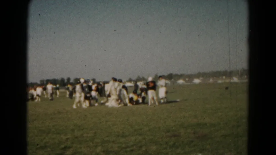Home-movie frame from the 1966 Hagerstown football game with players standing and crouching after a play on the field.