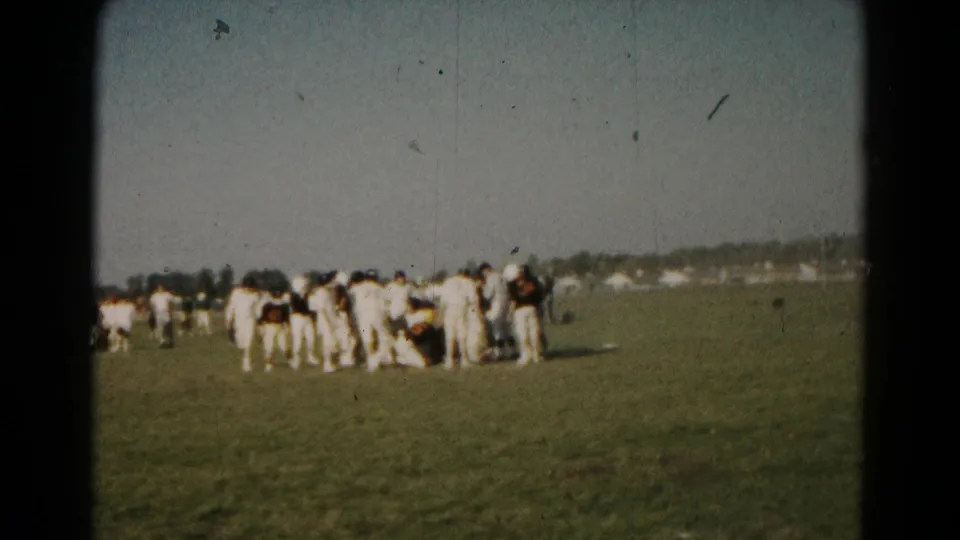 1966 Hagerstown 8mm frame showing players gathered around a football pileup, with open field and tree line in the distance.