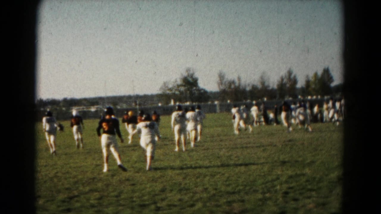 1966 Hagerstown home-movie frame showing field-sport players running away from the camera on a grass pitch.