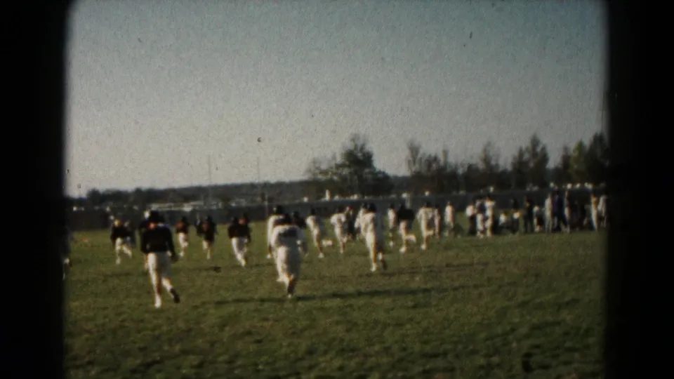 Wide 8mm view of a 1966 Hagerstown field game, with players spread across the grass and spectators beyond them.