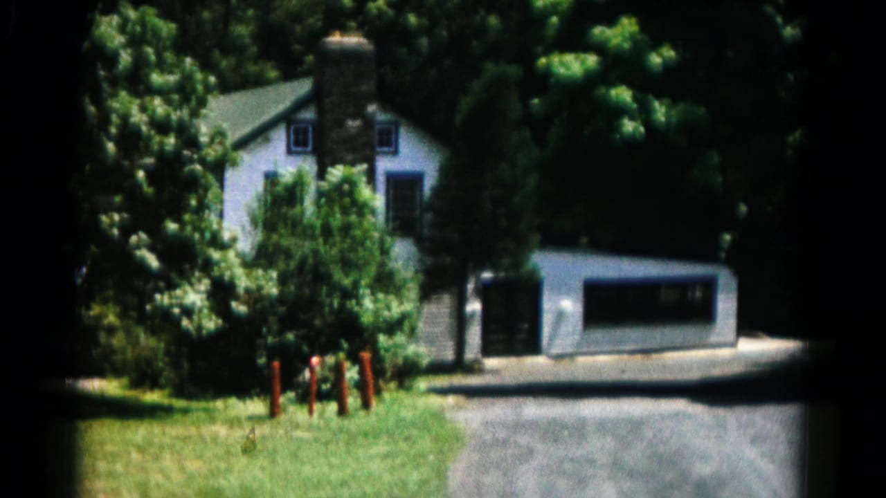 1966 Hagerstown-area home-movie frame showing a white house behind grass, trees, a driveway, garage, stone chimney, and red posts.