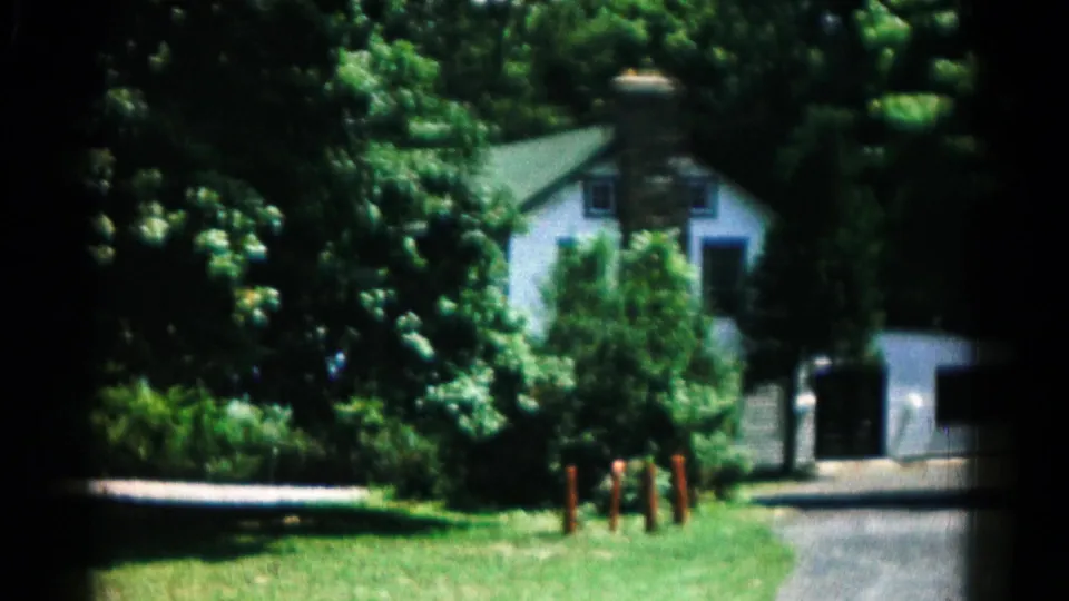 1966 Hagerstown, Maryland footage showing a leafy residential exterior with a white house, garage, driveway, lawn, and red posts.
