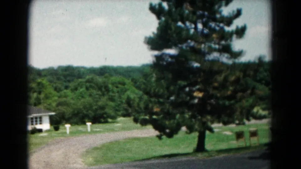 1966 Hagerstown residential exterior with a white house, curving gravel drive, pine tree, mailboxes, and green lawn.