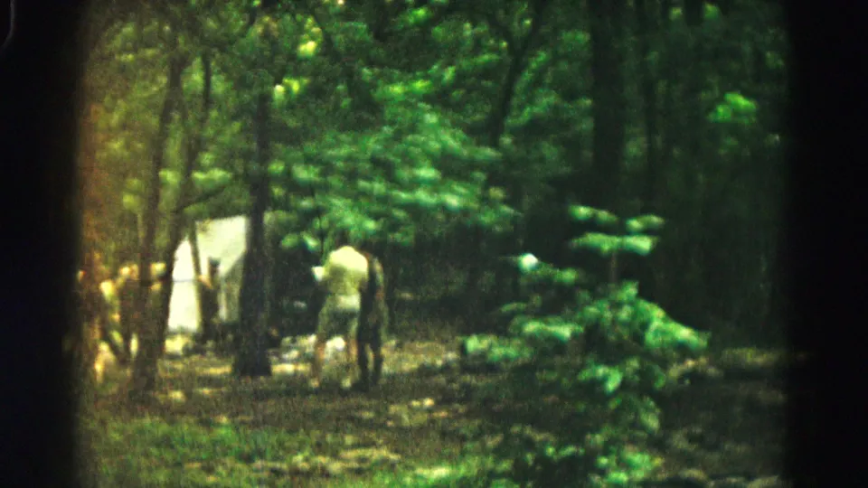 A 1966 home-movie view near Hagerstown showing a person walking through trees beside a white tent in a forest clearing.