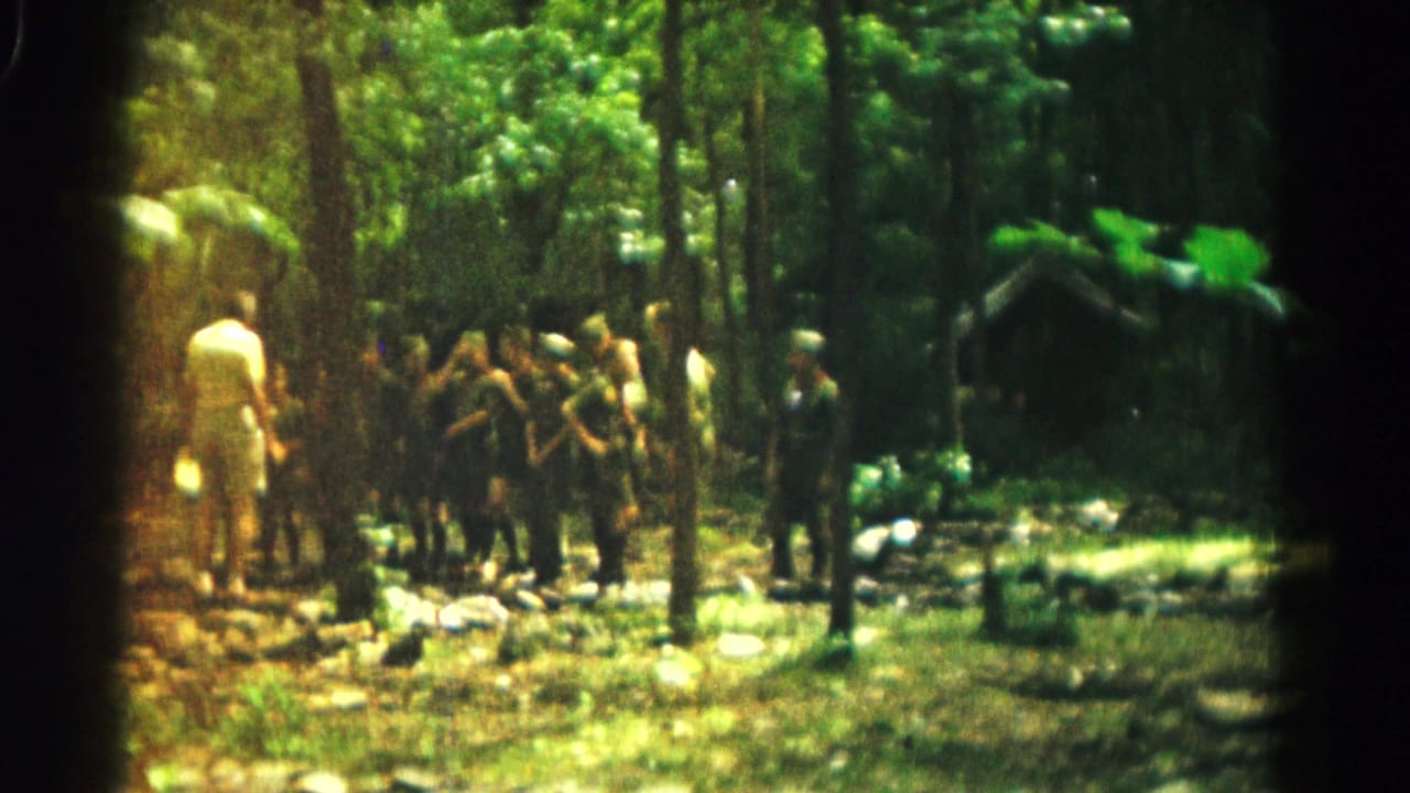 1966 8mm frame from Hagerstown, Maryland, showing boys gathered near an adult leader in a forest clearing.