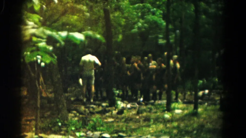 A 1966 Hagerstown 8mm frame shows boys and an adult in a dense wooded area, likely part of an outdoor camp activity.