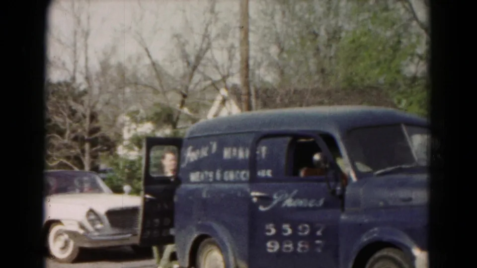1966 Hagerstown frame with a woman by the open side door of a blue Frank's Market van and a white classic car behind it.