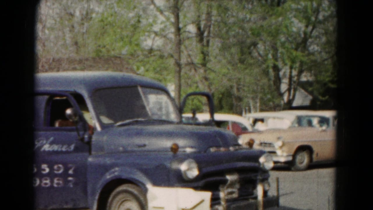 1966 Hagerstown home-movie frame with a blue marked delivery van and period cars parked near trees.