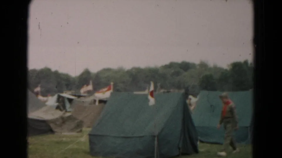 A uniformed scout-style figure walks near green canvas tents in the 1966 Maryland camp footage.