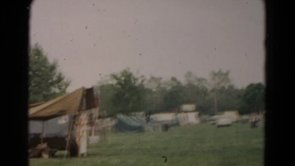 1966 Hagerstown home-movie frame showing a grassy field with tents, trees, and a canvas awning at left.