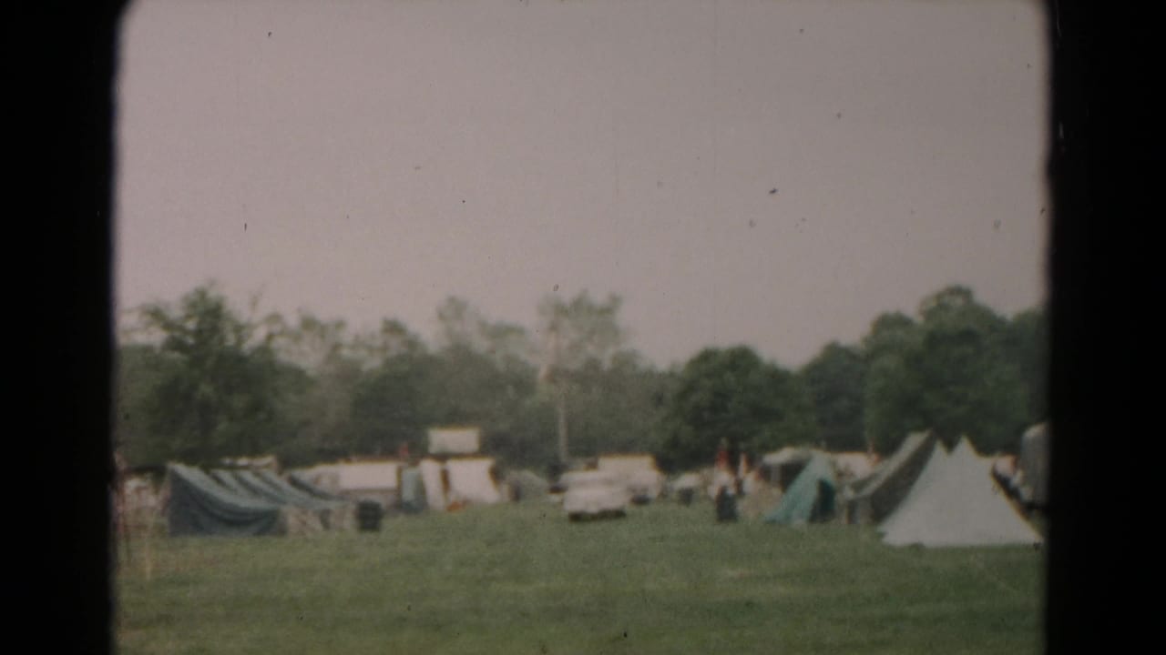 1966 Hagerstown camping scene with tents, parked cars, trees, and distant people in an open field.