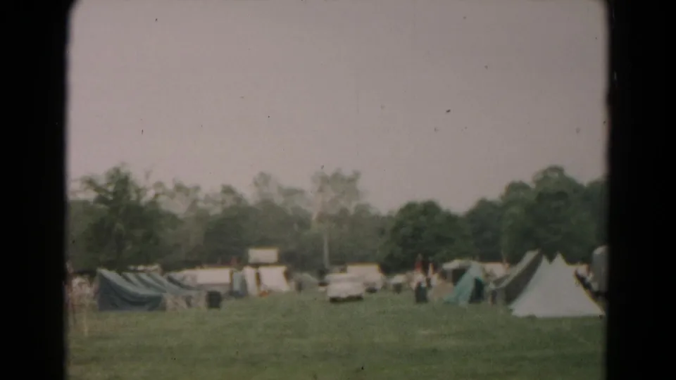 1966 Hagerstown camping scene with tents, parked cars, trees, and distant people in an open field.