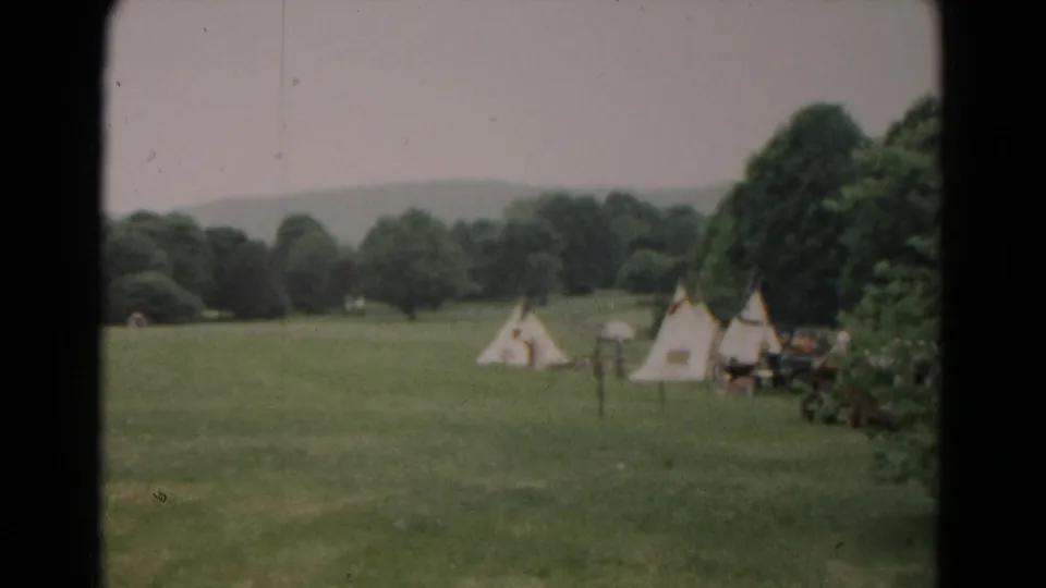 Wide 1966 Hagerstown view of a grassy field, scattered canvas tents, trees, and a distant hill under a pale sky.