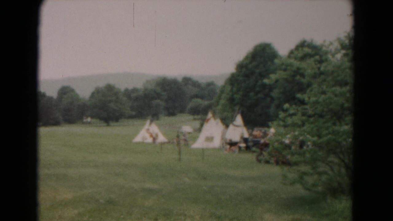 1966 Hagerstown home-movie frame showing a small tent cluster by trees, open grass, and distant hills in soft 8mm color.