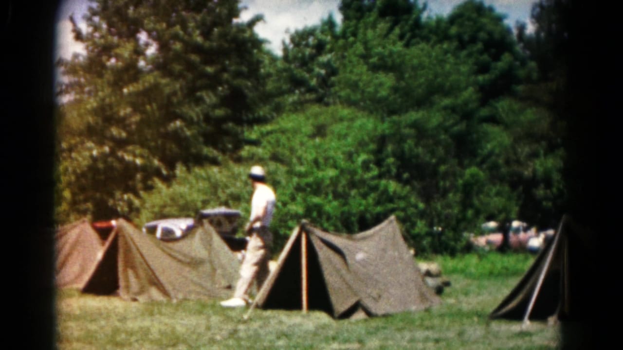 1960s campsite scene in Hagerstown with an adult walking among canvas tents, trees, and parked cars in the background.