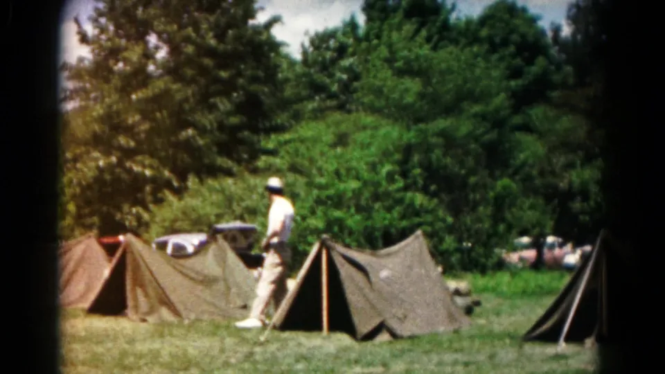 1960s campsite scene in Hagerstown with an adult walking among canvas tents, trees, and parked cars in the background.