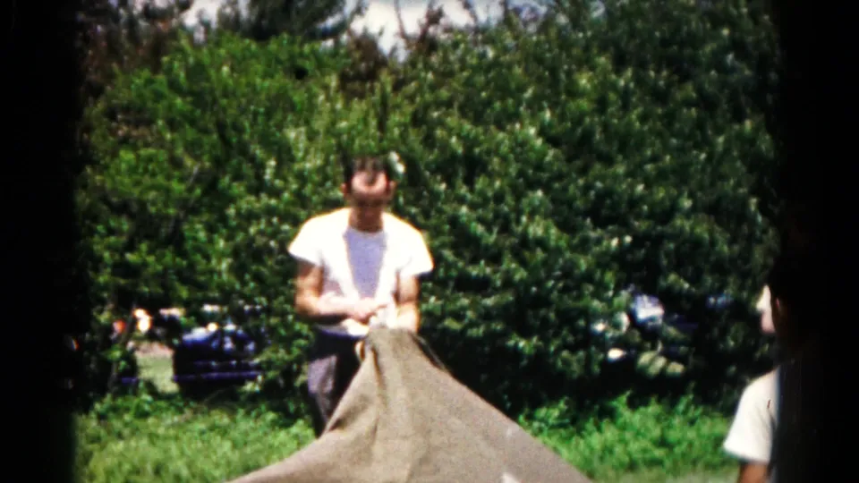 Near the end of the clip, the man holds the gathered top of the sack while standing before dense greenery and a partially visible car.