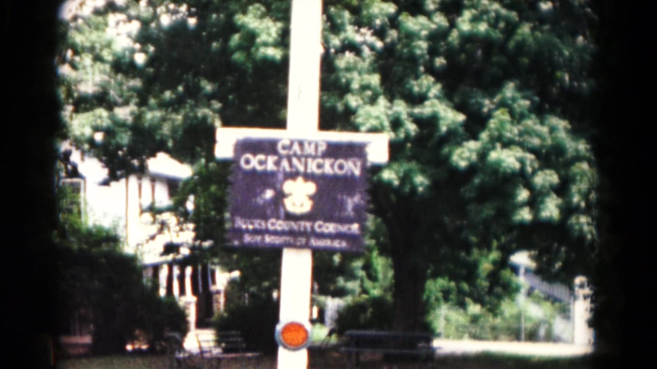 1966 Hagerstown frame showing a dark Camp Ockanickon sign on a white pole, with trees and a pale building in the background.
