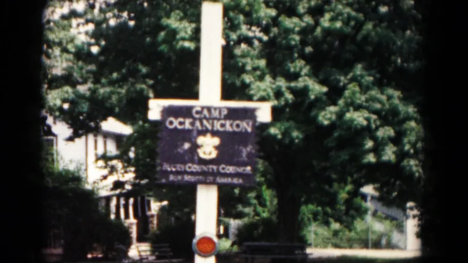 Final 1966 Hagerstown frame holding on the Camp Ockanickon sign, scout emblem, white pole, trees, and background building.