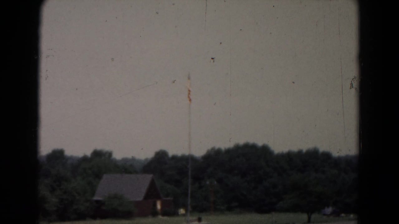 Soft rural view with small red building, tree line, flagpole, and dark frame edges.