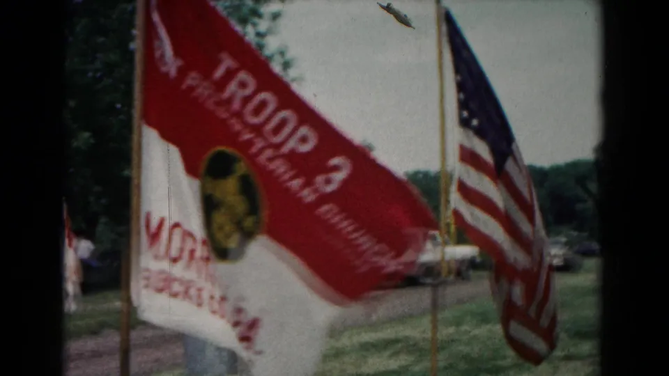 1966 Hagerstown scouting camp view with a red and white Troop 3 flag and an American flag near parked cars.